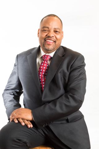 A young man with short hair smiles outdoors, captured in warm sunlight.